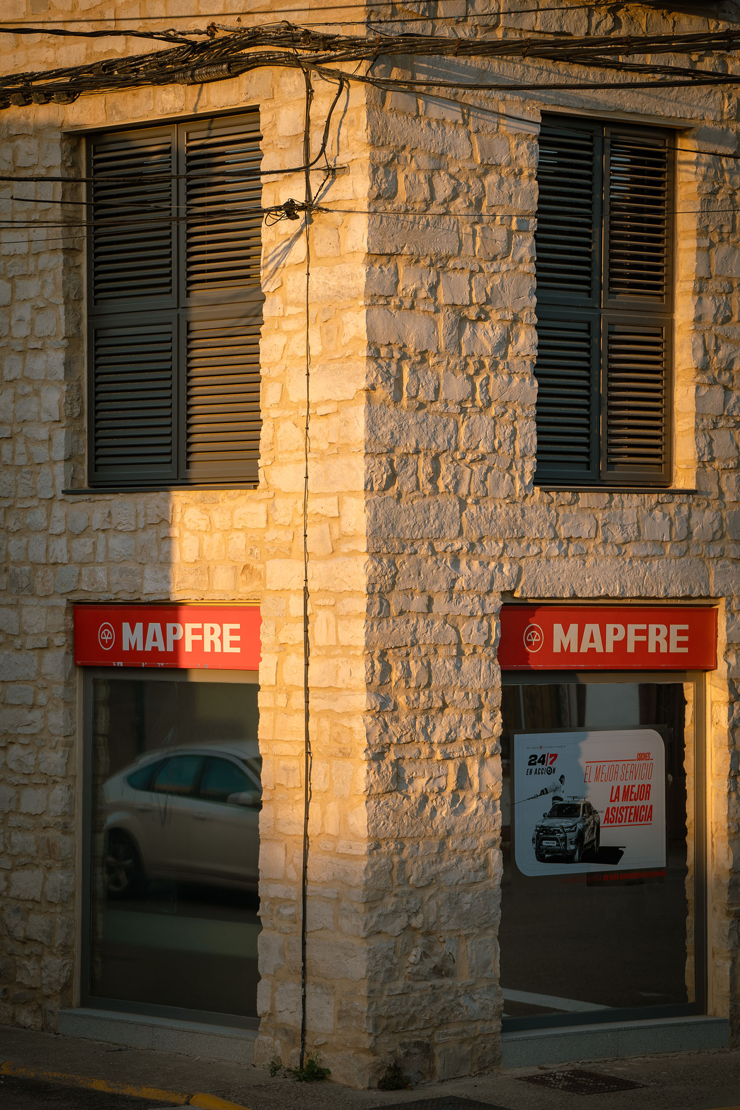 Esquina del edificio mostrando la textura de la piedra y los rótulos corporativos rojos de Mapfre